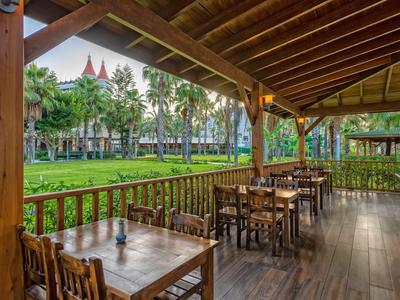 Terrasse en bois couverte avec tables et chaises surplombant un jardin vert et un bâtiment hôtelier.