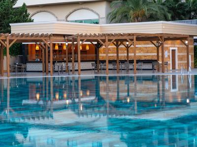 Outdoor pool with wooden pavilion and seating by a hotel surrounded by greenery.