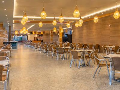 Spacious restaurant with wooden walls, hanging lights, and tables with chairs.