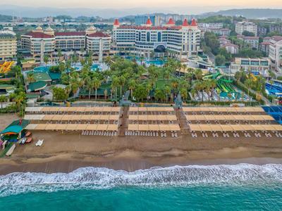 A beachfront hotel resort with palm trees, sun loungers, and a sandy beach beside a turquoise sea.