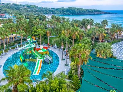 Colorful water slides and pool surrounded by palm trees near the sea.