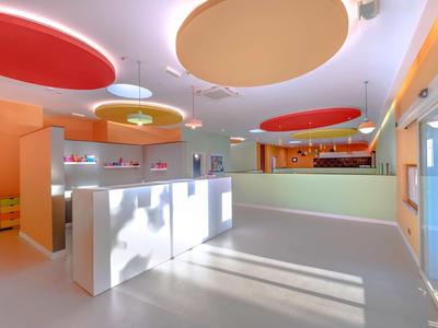 Bright hotel lobby with white reception desks, colorful round ceiling lights, and large windows.