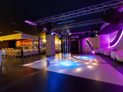Club d'hôtel moderne avec piste de danse colorée et espace lounge sous un éclairage doux.
