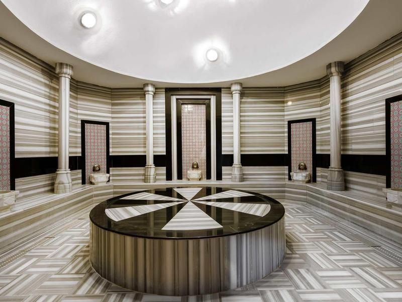 Circular room with patterned tiled floor and central round platform, wooden doors, and striped walls.