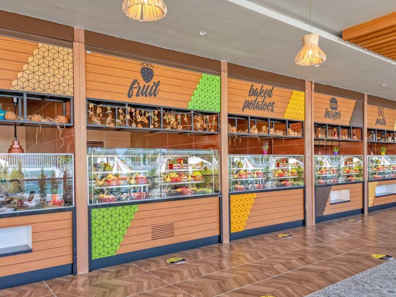Indoor market with bright orange stalls selling fruit and other goods under warm lighting.