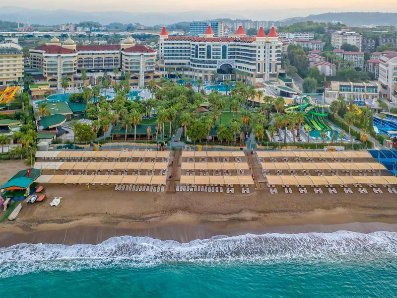 A beachfront hotel resort with palm trees, sun loungers, and a sandy beach beside a turquoise sea.