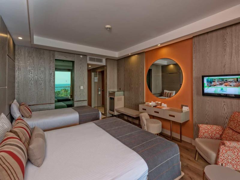 Modern hotel room with two beds, desk, armchair, and flat-screen TV.