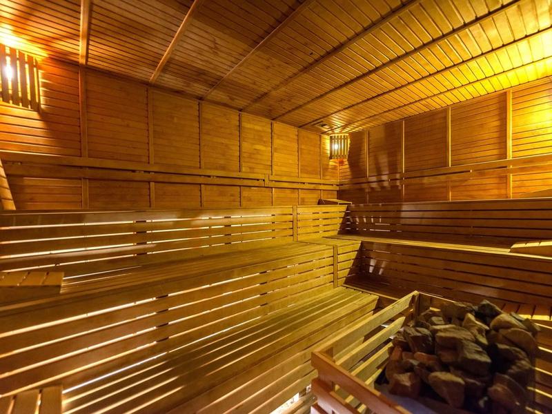 Interior of a warmly lit wooden sauna with tiered benches and a stone heater.