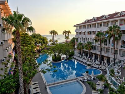 Ein Hotel mit großen Pools, Palmen und Sonnenliegen bei Sonnenuntergang am Meer.