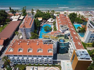 Aerial view of a hotel with red roofs, pools, and a view of the beach and sea.