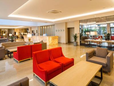 Bright hotel lobby with red and gray sofas, plants, and large window overlooking the street.