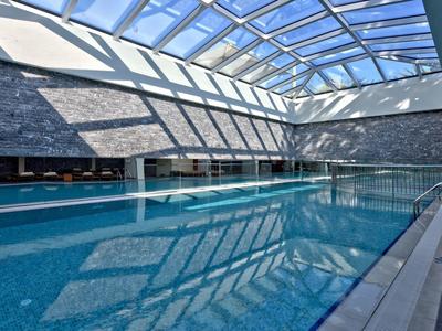 Indoor swimming pool with large glass roof and natural light in a modern hotel.