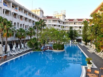 Large hotel pool with sun loungers and palm trees surrounded by a multi-story building
