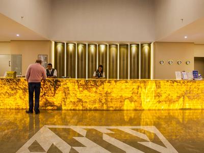 Mostrador de recepción marmoleado amarillo en un hotel con un hombre delante y un empleado detrás.