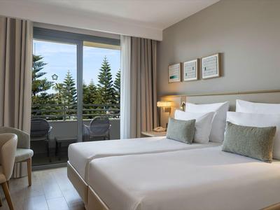 Habitación de hotel moderna con dos camas, escritorio y balcón con vista a los árboles.