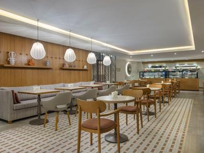 Área de comedor moderna en hotel con paredes de madera, bancos acolchonados y luces colgantes.