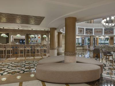 Un elegante área de lounge en un hotel con bar, numerosos asientos y suelo de mármol.