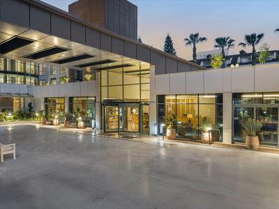 Entrada moderna del hotel con gran fachada de vidrio y elegante iluminación exterior al anochecer.