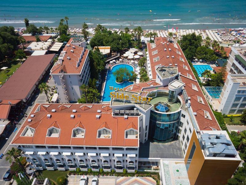 Aerial view of a hotel with red roofs, pools, and a view of the beach and sea.