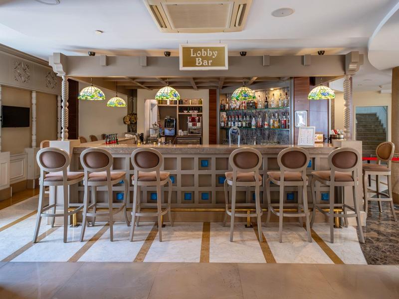 Bright bar area with counter, eight bar stools, and decorative lamps in a modern hotel.