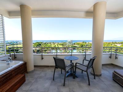 Balcone con vasca idromassaggio, tavolo e due sedie con vista sul mare e sulla vegetazione.