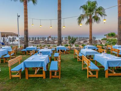 Ristorante all'aperto con tovaglie blu, mobili in legno e vista sul mare al tramonto.