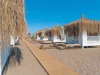 Fila di bungalow bianchi con tetti di paglia e lettini sulla spiaggia sabbiosa sotto un cielo blu.