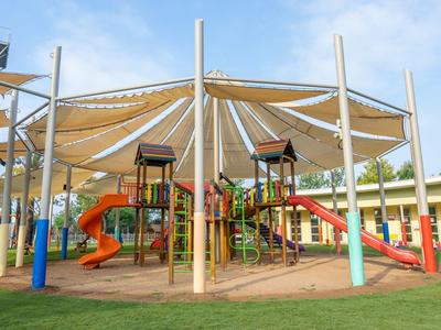 Parco giochi con scivoli e struttura per arrampicata sotto un grande tendone in una giornata soleggiata