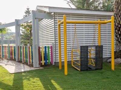 Parco giochi all'aperto con altalena gialla e recinto colorato accanto a un edificio bianco