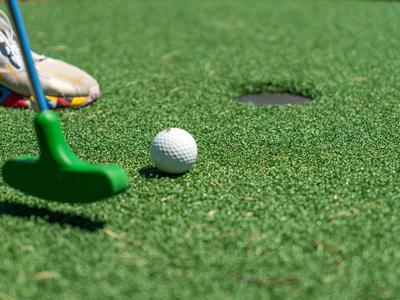 Putter da golf verde e pallina bianca sull'erba vicino alla buca.