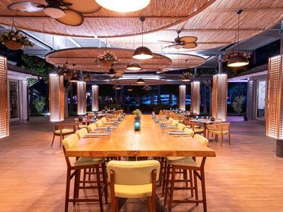 Grande ristorante modernamente illuminato con un lungo tavolo di legno e sedie di legno