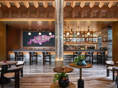 Area bar moderna dell'hotel con pannelli in legno, tavoli alti e illuminazione indiretta.