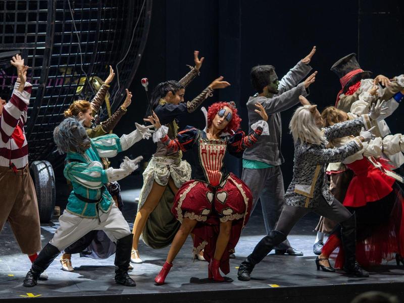 Compagnia teatrale in costumi colorati esegue una scena drammatica sul palco.