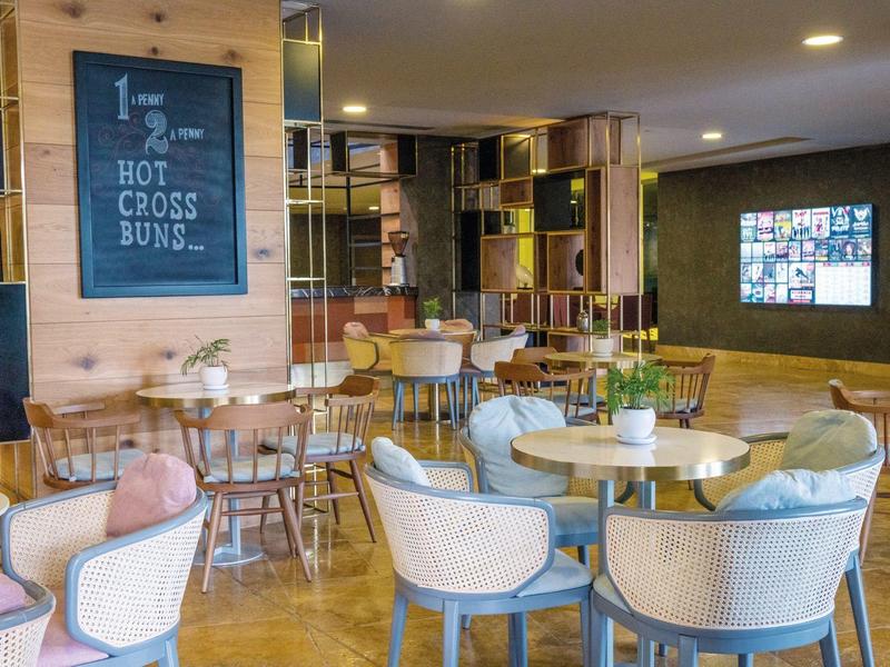 Area lounge dell'hotel moderna con sedie, tavoli e uno schermo televisivo.