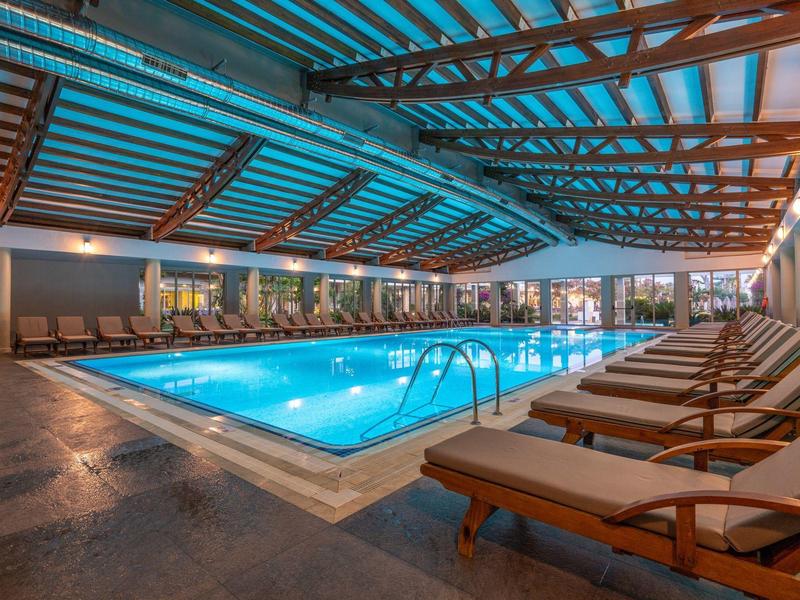 Piscina coperta riscaldata con lettini sotto un tetto trasparente.