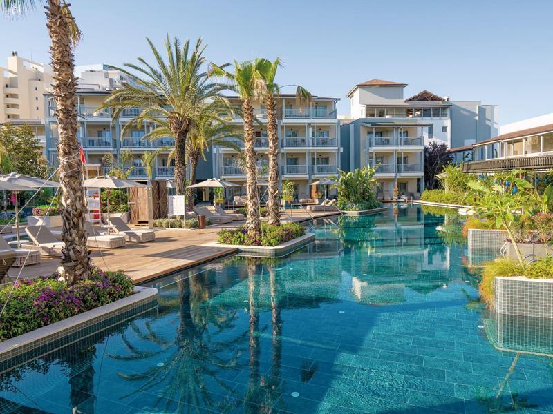 Area piscina moderna dell'hotel con palme, lettini e architettura elegante alla luce del giorno.