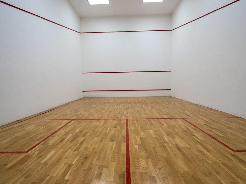 Campo da squash vuoto con pavimento in legno e pareti bianche, linee rosse che delimitano il campo.