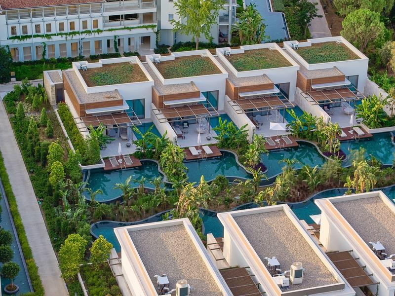 Vista aerea di un resort con ville moderne, ciascuna con piscina privata e giardino.