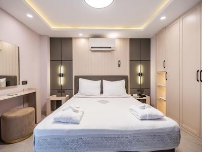 Habitación de hotel moderna con cama grande, mesitas de noche y armario en colores neutros.