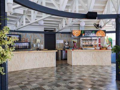 Area interna moderna di un bar dell'hotel con due banchi in legno, distributori di bevande e piante decorative.