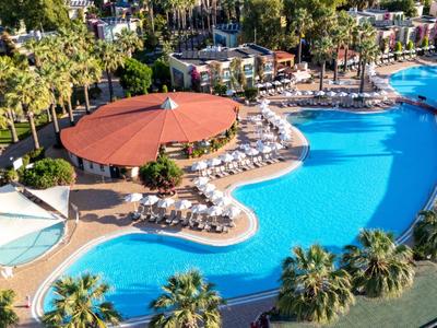 Groot hotelzwembad met palmbomen, parasols en ligstoelen in een zonnige omgeving.