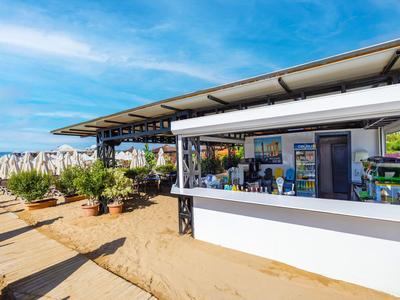 Strandbar met open raam, palmbomen en blauwe lucht op het zandstrand.