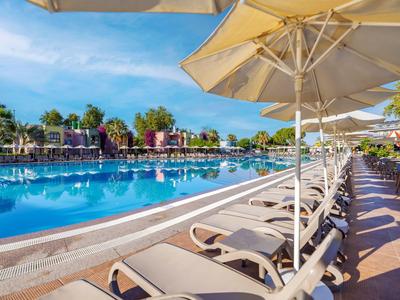 Groot buitenzwembad met ligstoelen en parasols bij een hotel onder een heldere lucht.