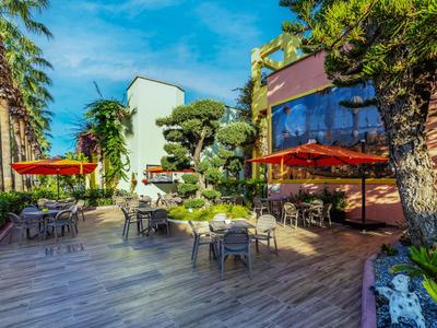 Buitenruimte van een hotel met tafels, stoelen en rode parasols onder een blauwe lucht.