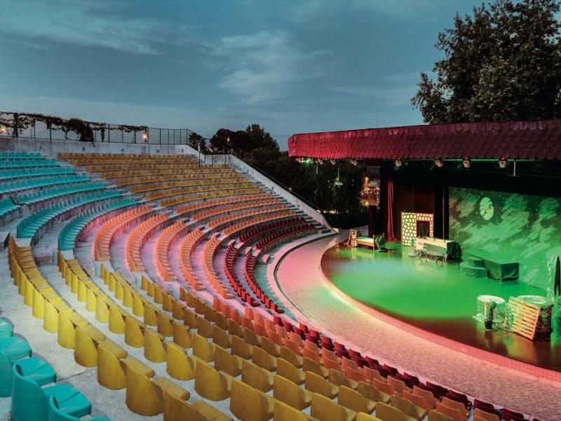 File di sedili colorati in un teatro all'aperto sotto un cielo nuvoloso.