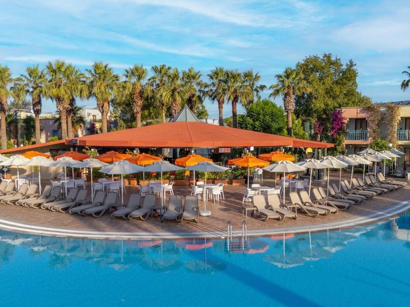 Grande piscina dell'hotel con lettini e ombrelloni arancioni circondata da palme.