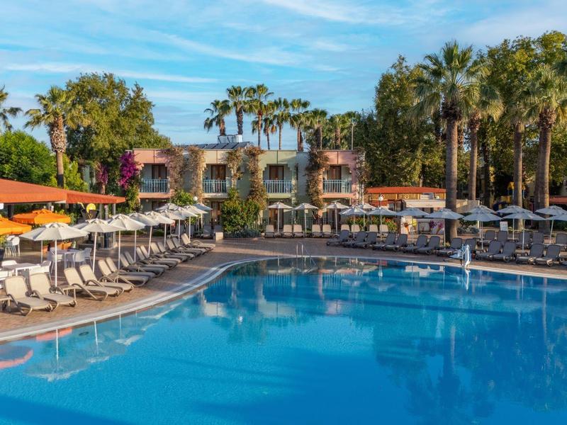 Grande piscina dell'hotel con lettini e palme sotto un cielo azzurro