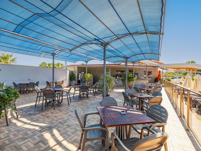 Terrazza coperta con tavoli e sedie in un'area esterna soleggiata di un hotel.