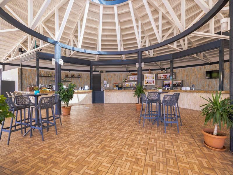 Interno di un moderno ristorante aperto con pavimento in legno e tavoli rotondi sotto una struttura in legno alta.