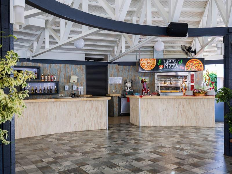 Area interna moderna di un bar dell'hotel con due banchi in legno, distributori di bevande e piante decorative.